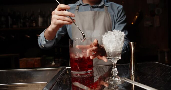 Professional bartender masterly creating a cocktail in modern bar. Experienced barman mixing red alchoholic beverage before serving - food and drink, nightlife close up 4k footage