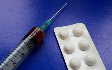 A syringe with medicine and tablets on a blue background.