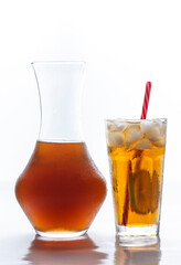 Iced tea with straw, ice cubes and sliced lemon and a glass bottle over white background