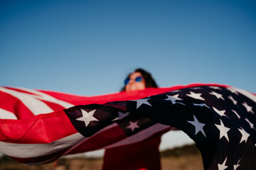 young woman holding United States flag outdoors at sunset. Independence day in America, 4th July...