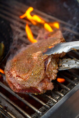 Rob Eye Steak being turned with tongs on BBQ with flames