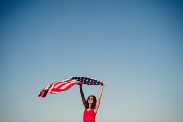 young woman holding United States flag outdoors at sunset. Independence day in America, 4th July...