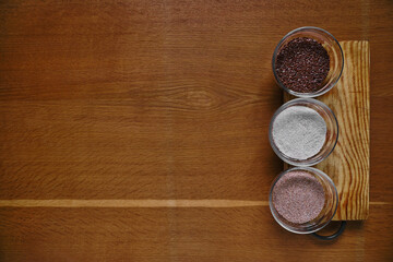 Top view of flax and bran set in glass bowls as healthy dietary food on wooden board and wooden background. Creative flatlay with cererals.
