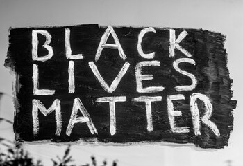 Young white girl painting Black Lives Matter text on glass window. Sign against racism, for human rights and freedom of all people. Black and white image.