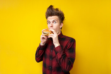 shocked guy eating a burger on a yellow isolated background, surprised hipster eating tasty fast food