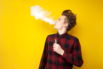 guy hipster smokes an electronic cigarette on a yellow isolated background, a man exhales a cloud of smoke and holds a device for smoking