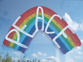 Painting of LGBT (Lesbian, Gay, Bisexual and Transgender) rainbow flag on window with the word Peace. Beautiful reflections of clouds in the glass