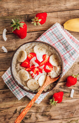 Quinoa porridge with coconut milk and fresh strawberries in a coconut bowl wooden rustic background. Healthy Lactose and Gluten Free Breakfast.