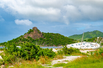 Fototapeta na wymiar Coastal landscape on tropical Caribbean island with old yacht shipwreck abandoned on shore. Land of lush green vegetation and mountains in background.