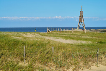 the beacon Kugelbake in Cuxhaven (Germany) seen behind green beach grass on a sunny spring afternoon with vivid blue sky