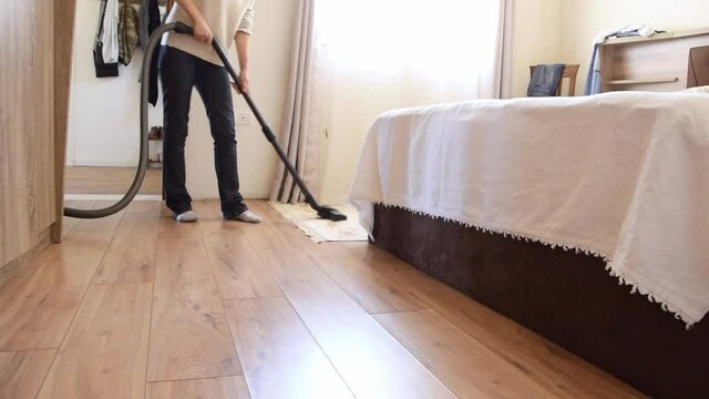 Adult woman cleaning bedroom with vacuum cleaner

