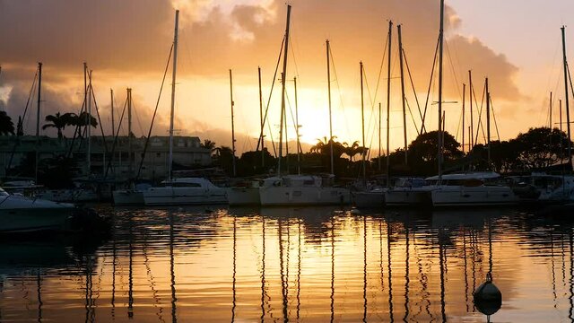 Dark reflections of yachts floating in the harbor during a colorful sunset in Guadeloupe slow motion