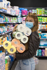 Young girl in supermarket in medical mask holds a lot of packages of toilet paper