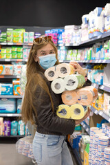 Young girl in supermarket in medical mask holds a lot of packages of toilet paper