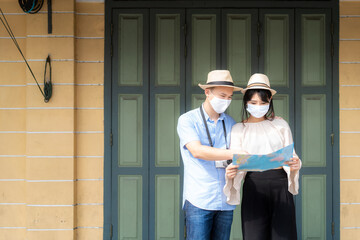 Plakat Asian couple happy tourists to travel wearing mask to protect from Covid-19 on they holidays and holding travel map in old town in Bangkok, Thailand