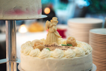 White wedding cake standing on festive table. Closeup of topper figurines of bride and groom. Wedding day concept.