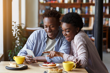 Fototapeta na wymiar Romantic times. Beautiful African American couple with smartphone on date in coffee shop
