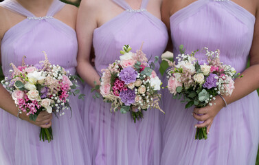 Three bridesmaids in lilac dresses hold bouquets in their hands without faces