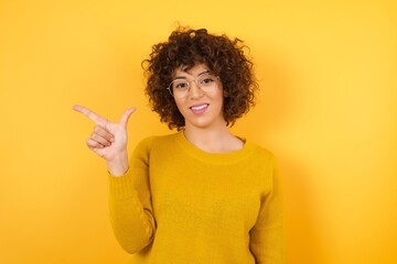 Young beautiful Cucasian businesswoman wearing yellow sweater and glasses standing against yellow background pointing up with fingers number eight in Chinese sign language BÄ.