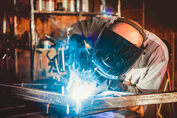 Welder working in the workshop. Welding a metal construction. Sparkles and combustion. Hard work.