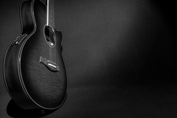 Retrato en blanco y negro de una hermosa guitarra electroacústica de pie sobre su costado, puede ver el estuche y parte del cuello, sobre un fondo oscuro, iluminando solo la guitarra.