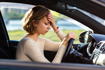 Exhausted woman driver feeling headache, sitting inside her car, keeping hand to head and feeling...