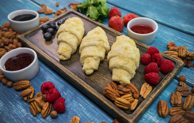 Raw croissants on the wooden desk surrounded by fruits and nuts