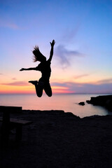 silhouette of a jumping girl in the sunset in the background the sea and a wonderful colorful sky