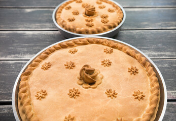 Two potato pies with edible decorations on top standing on the wooden table