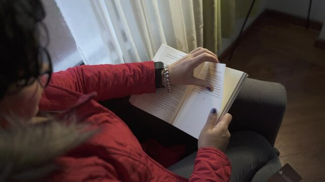 Mujer leyendo un libro, da vuelta a la p&aacute;gina y termina un cap&iacute;tulo. Deja de leer y mira  a trav&eacute;s de la ventana, al final empieza a reflexionar.