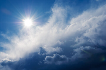 bright natural sun behind dramatic dark clouds in blue sky