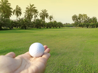 Hand holding a golf ball, background of golf course