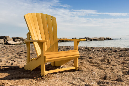 a Yellow Adirondack wooden beach chair on a sandy beach