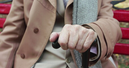Wrinkled old man's hands clutching on crutch while resting on a street bench