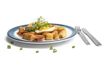 a fried egg sunny side up on a blue plate with potatoes bacon asparagus and bread isolated on white