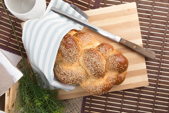 a braided loaf of sesame challah bread on a wooden cutting board covered in cloth isolated on white
