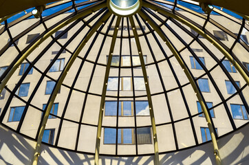 View through the glass dome roof of modern corporate building with windows and sky reflections.