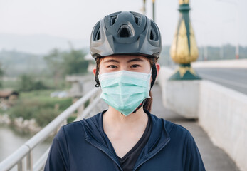 Portrait of young woman wearing a mask while riding a bicycle outdoor for protect and prevent the spread of virus. Conceptual of new normal lifestyle, everybody should wearing a mask when go outdoor.