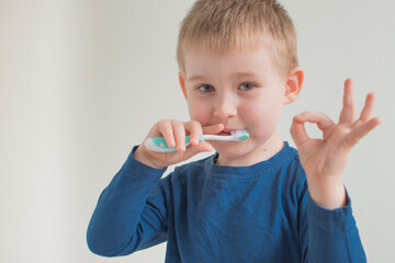 Portrait of little boy brushing teeth on light background and show ok sign. Dental hygiene. Copy space for text