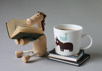 enjoyment of reading books, wooden horse toy, coffee mug with mini books on the grey background.