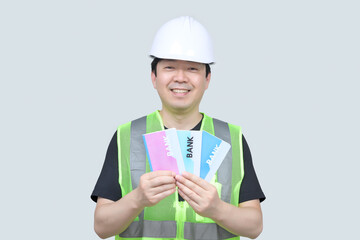 A middle-aged Asian engineer holding a bank passbook in his hand on a gray background.
