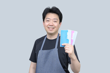 A middle-aged Asian man holding a bank passbook in his hand on a gray background.