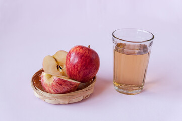 Cut and whole red Apple in a wicker plate and a glass of Apple juice on a pink background