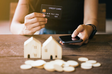 Hold a smartphone and a credit card and have a picture of a replica home on the front. Credit card concept.  Focus on a simulated wooden house. smartphone and a credit card. Photo noise and grains
