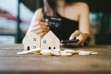 Hold a smartphone and a credit card and have a picture of a replica home on the front. Credit card concept.  Focus on a simulated wooden house. smartphone and a credit card. Photo noise and grains
