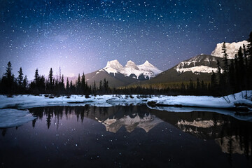 Alpine night scene with sky full of stars and mountain reflected in water surface, shot in Canmore, Alberta, Canada