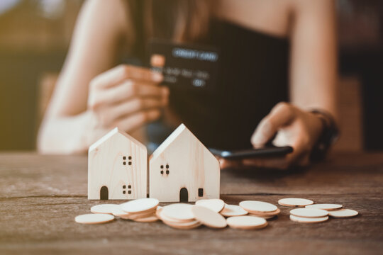 Hold a smartphone and a credit card and have a picture of a replica home on the front. Credit card concept.  Focus on a simulated wooden house. smartphone and a credit card. Photo noise and grains
