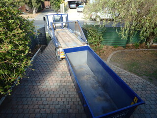 Truck (Lorry)  delivering a empty waste skip bin to a suburban house.