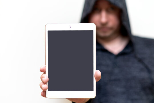 Young caucasian man in dark gray sweatshirt with hood holds tablet pc computer with blank screen for copy space isolated on white background. Concept of technology