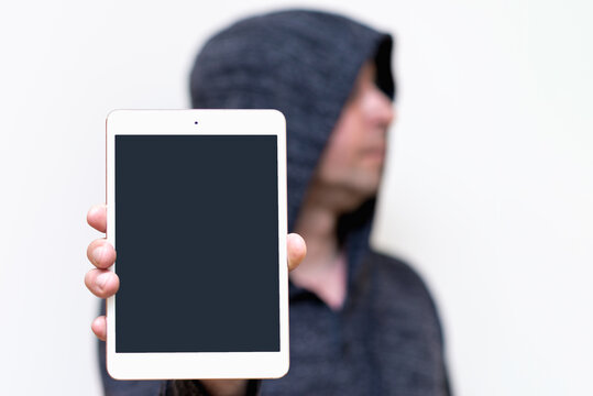 Young caucasian man in dark gray sweatshirt with hood holds tablet pc computer with blank screen for copy space isolated on white background. Concept of technology